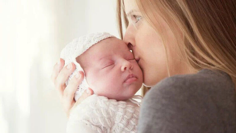 A mother kisses the forehead of her newborn baby. 