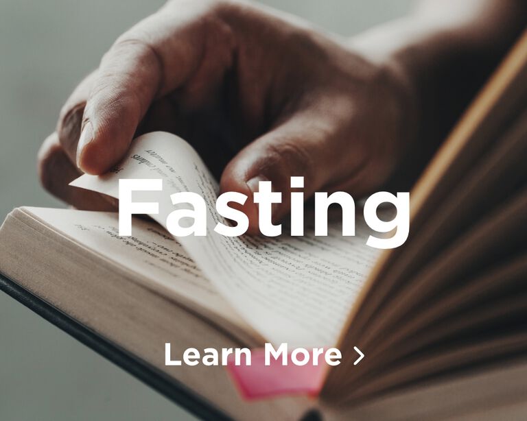 A person's hand holding a Bible turning a page. Image links to Fasting page.