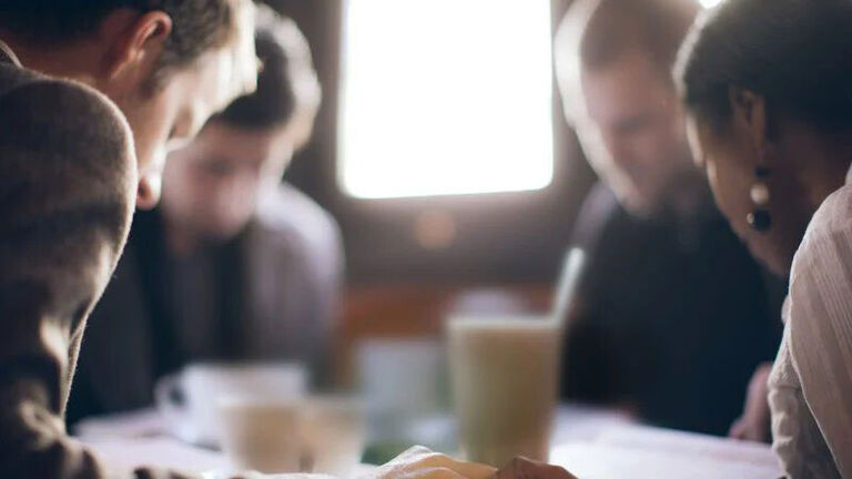 Four friends bow their heads in prayer before a meal. 