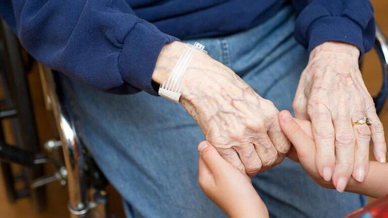 A young child holds the hands of his grandmother. 