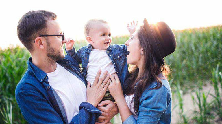 A family of three laughs in a cornfield. 