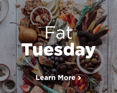 An assortment of fresh fruit, nuts, artisanal cheeses, and crackers laid out on a white wooden table. Image links to Fat Tuesday page.