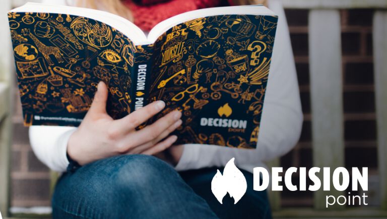 A smiling teenage girl sits on a tan couch in her living room while reading through Dynamic Catholic's confirmation program, Decision Point