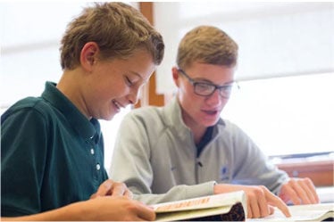 Two middle school boys sit and read together their Dynamic Catholic Decision Point workbooks 
