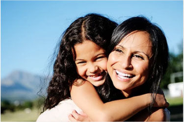 Mother gives daughter a piggy back ride. Mountains visible in the distance. 